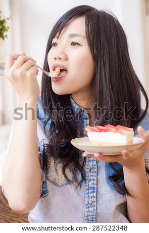 Asian smiling woman wearing jean shirt biting the piece of tasty strawberry cake, Strawberry fruit dessert