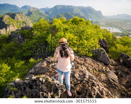 Hiker woman with backpack and camera relaxing on top of a mountain and enjoying sunrise