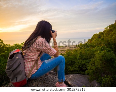 Hiker woman with backpack and camera relaxing on top of a mountain and enjoying sunrise