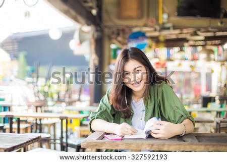 Asian woman reading a book while sitting on wooden table smiling outdoor