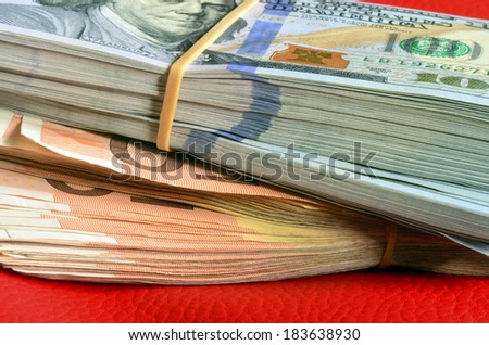 Stacks of ten thousand american dollars and five thousand euro on red leather background.