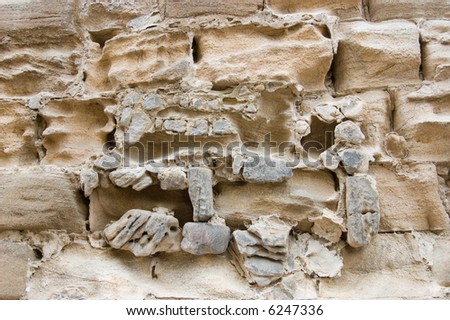 Weathered ancient stone wall, the soft stone and masonry eroded by the passage of time and the effects of rain and wind
