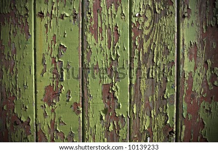 Green paint peeling from a wooden panel door showing the wood grain and old red painted surface