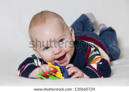 Happy baby boy lying on his stomach and playing with toy and smiling.