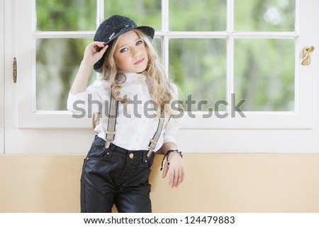 Little girl in stylish look wearing black trousers, braces and white blouse.