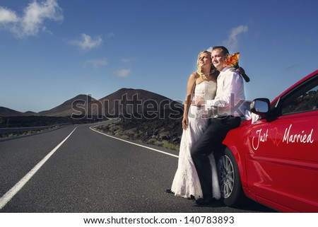 Newlyweds on the road next to the red car with inscription 