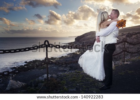 The groom lifted the bride on hands and kissing near the ocean shore at sunset in Canary Islands.