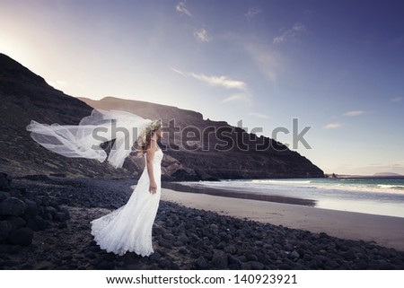 A bride standing in the ocean, the veil fluttering in the wind in Canary Islands.