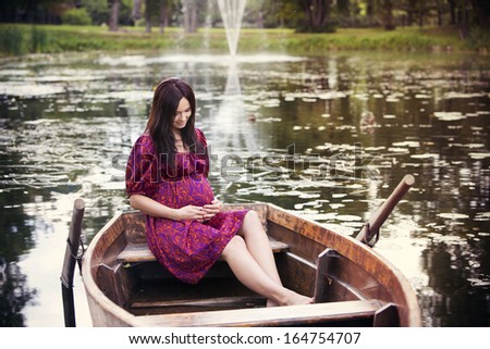 Happy pregnant woman sitting in a boat and look at her belly.
