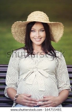 Happy pregnant woman with beautiful eyes sitting in a chair embracing her belly.