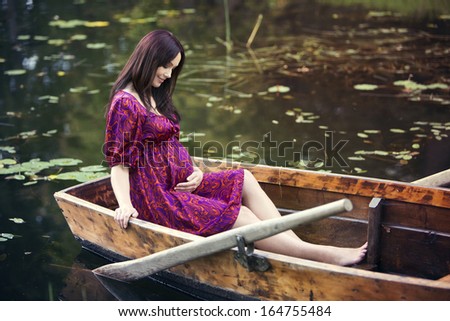 Happy pregnant woman sitting in a boat and embrace her belly.