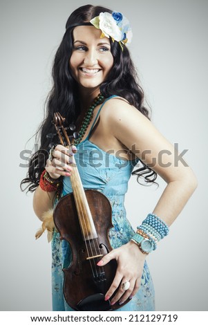 Beautiful girl with long dark hair wearing a blue clothes and accessories standing in studio with violin in hands.