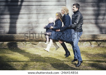 Happy family - mom, dad and two daughters sitting in the row behind one another on the beam out in Autumn.