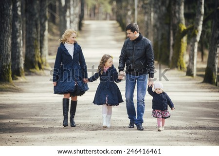 Happy family - mom, dad and two daughters holding hands go on the road through the alley in Autumn outdoors.