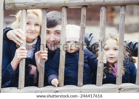 Happy family - mom, dad and two daughters playfully looks through a fence outdoors in Autumn.