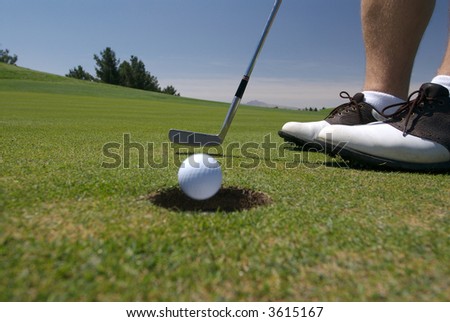Golfer putting as ball rolls into hole