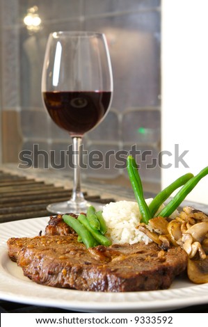 Cooked Rib-eye meal rice green beans and mushrooms close up with red wine out of focus shot from a low level room for text