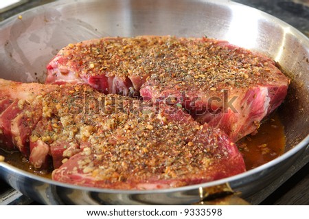 Raw seasoned rib-eye in a stainless steel frying pan waiting to be cooked