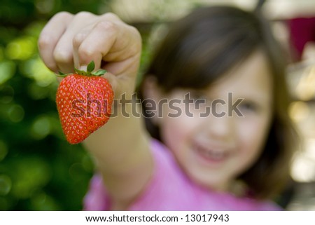 Young girl holding fresh strawberry in hand, her face out of focus