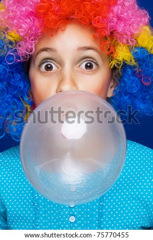 Young girl with party wig blowing bubble gum balloon