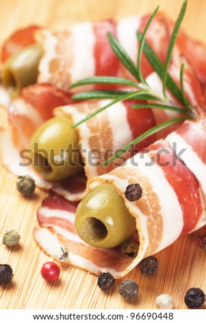 Slices of rolled bacon with green olives, rosemary and peppercorn