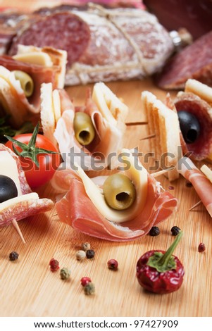 Tasty bites with toasted bread, prosciutto and olives