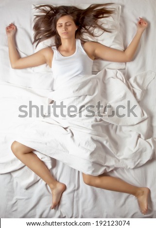 Young girl sleeping in bed on white sheets, shot from above