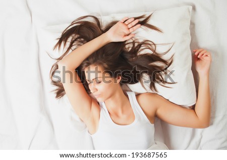 Young girl sleeping in bed on white sheets, shot from above