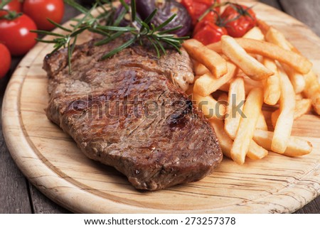 Beef rib-eye steak with french fries on wooden board