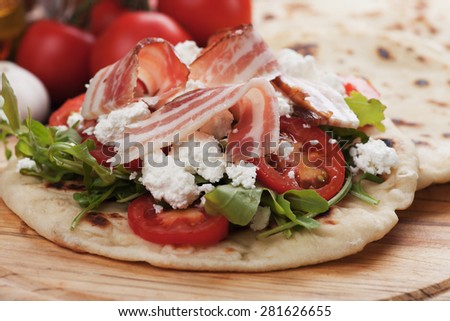 Piadina romagnola, italian flatbread sandwich with rocket salad, mozzarella cheese and pancetta bacon