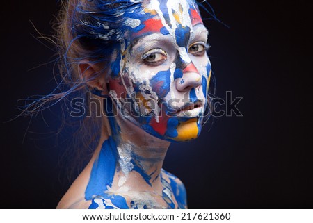 Portrait of a woman with face art.  who is posing covered with blue, red paint