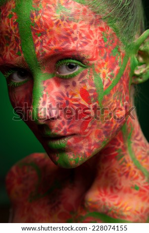 emotional woman with red multi lines and green hair. red flowers face art and body paint