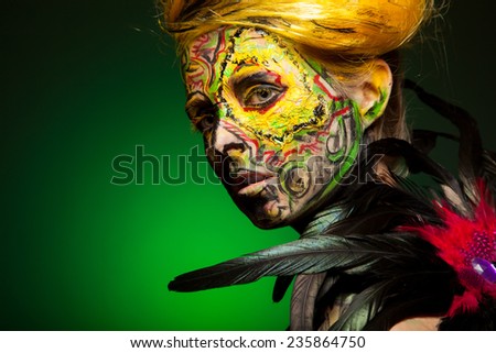 woman with face-art and body art paint. Yellow hair and red painted hand. Like bird. Feather decorated