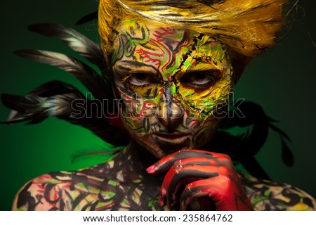woman with face-art and body art paint. Yellow hair and red painted hand. Like bird. Feather decorated