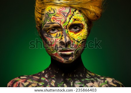 Woman posing in studio. Body and face art. Painted girl. On green background. Like bird. With red hand and yellow hair.