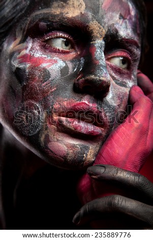 Woman painted with face art and body art. Portrait, color paint on face. Red and black background. Red hand
