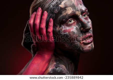 Woman painted with face art and body art. Portrait, color paint on face. Red and black background. Red hand