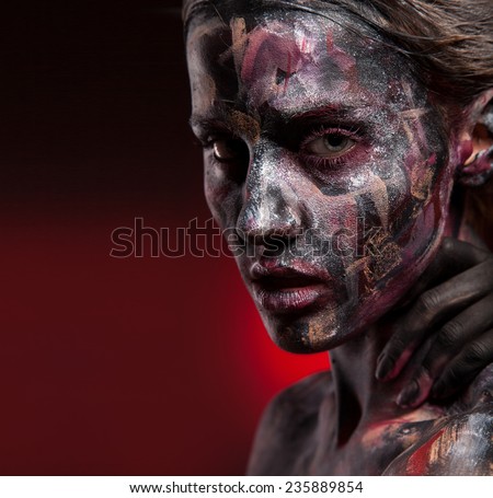 Woman painted with face art and body art. Portrait, color paint on face. Red and black background