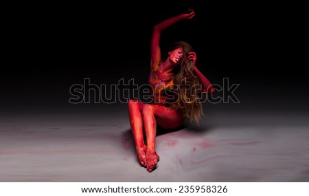 Sport woman in red posing in studio. With body art and face art. Painted body. Yoga. Fit woman doing stretching exercises