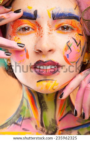 Beautiful fashion woman with bright color face art and body art. Paint on face. Posing in studio. Creative portrait on yellow background.