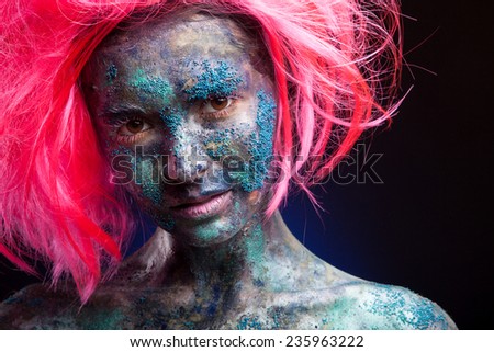Woman with  pink wig hair. Creative portrait with face art and body art. Painted face. On dark background.