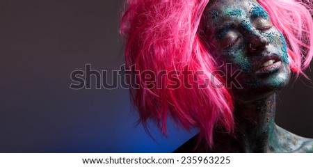 Woman with  pink wig hair. Creative portrait with face art and body art. Painted face. On dark background.