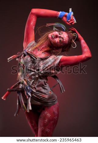 Young woman with creative face-art over dark red background. sensual girl with colorful bodyart. Creative hat and dress.