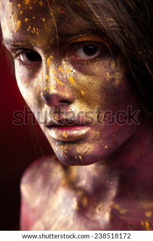 Girl with gold paint on face with face art and body art. Black hair. Portrait of sexy woman on dark background