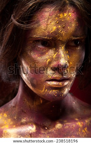 Girl with gold paint on face with face art and body art. Black hair. Portrait of sexy woman on dark background