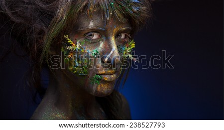 Girl with unusual body-art and face-art. Dark blue background. Color paint on face.
