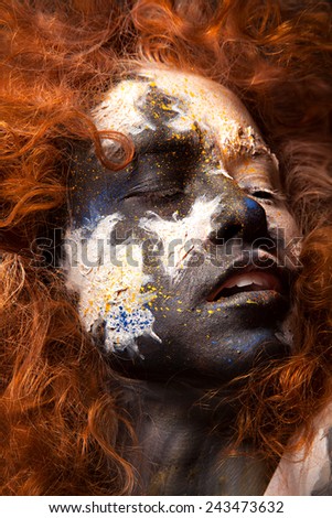 Red haired woman with face art and creative make up. Curly hair style. Black and white face art. Fantasy painted girl. Masquerade