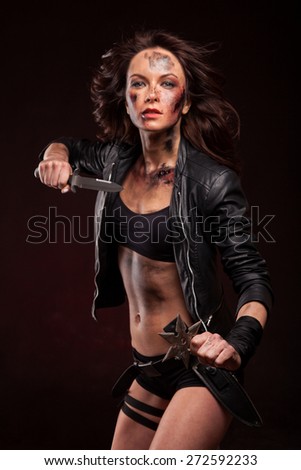 Woman holding a sharp knife with blood drops on face. Riot girl in leather jacket.