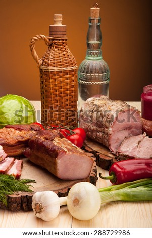 Smoked meat raw bacon and sausages with vegetables and salad with bottles of alchohol vodka and wine