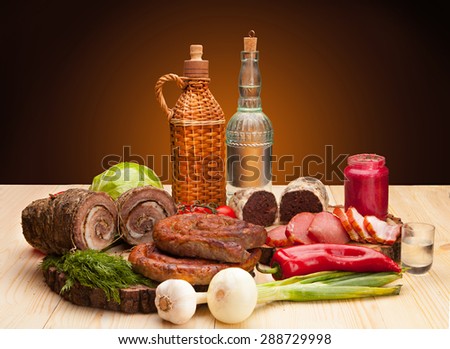 Smoked meat raw bacon and sausages with vegetables and salad on wooden background with bottles of alchohol vodka and wine